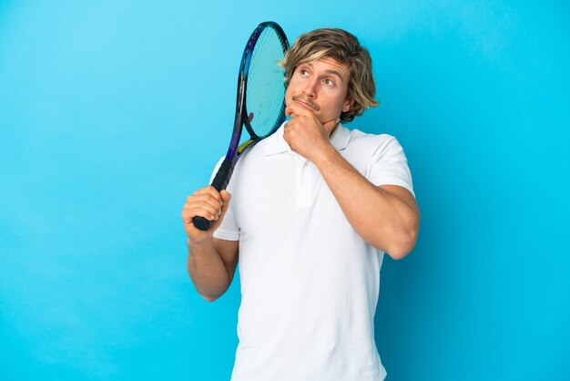 Blonde tennisspeler man geïsoleerd op blauw twijfels en denken