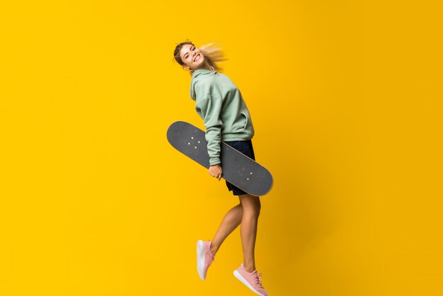 Blonde tiener skater meisje springen geïsoleerd op geel