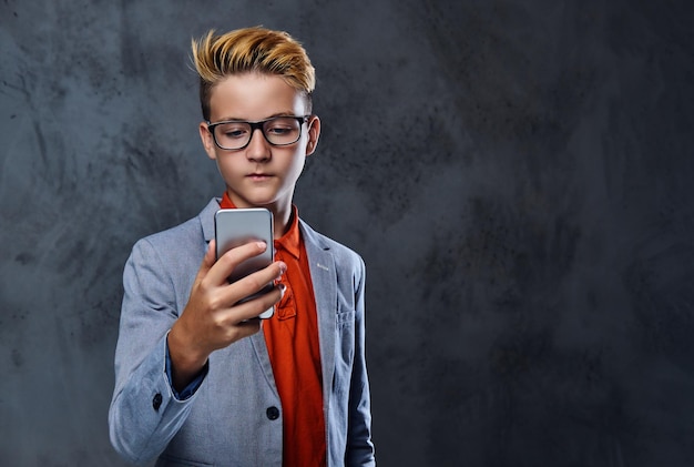 Blonde tienerjongen in een jas en bril houdt smartphone vast.