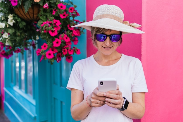 Blonde toerist in casual outfit legt kleurrijke gebouwen vast tijdens het sms'en met de telefoon