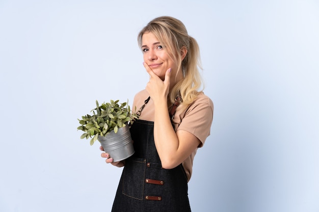 Blonde tuinmanvrouw die een installatie over geïsoleerde muur houdt die een idee denkt