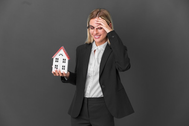 Blonde Uruguayan girl holding a house toy isolated on black background laughing