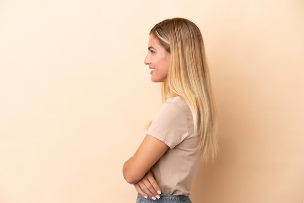 Blonde Uruguayan girl isolated on beige background in lateral position