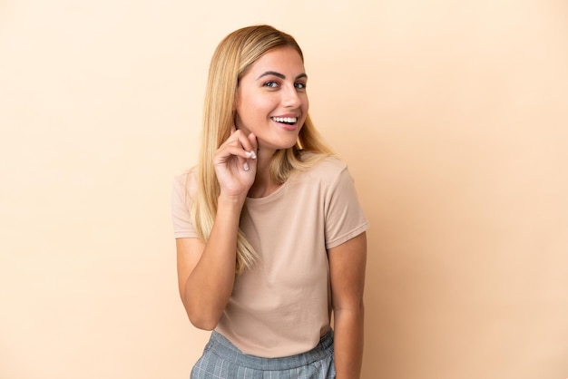 Blonde Uruguayan girl isolated on beige background laughing