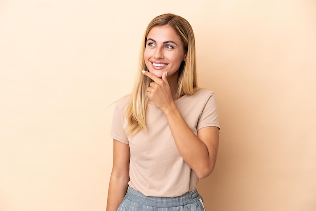 Blonde Uruguayan girl isolated on beige background looking to the side and smiling