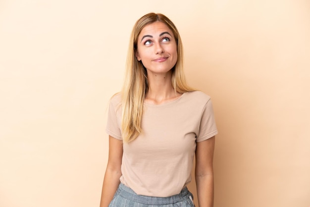 Blonde Uruguayan girl isolated on beige background and looking up