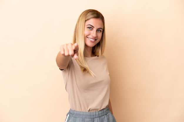 Blonde Uruguayan girl isolated on beige background pointing front with happy expression