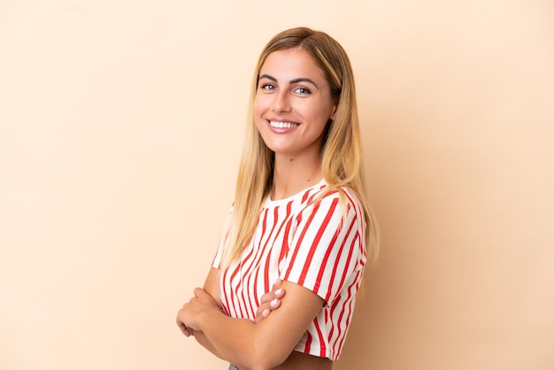 Blonde Uruguayan girl isolated on beige background with arms crossed and looking forward