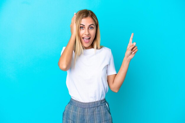 Blonde Uruguayan girl isolated on blue background surprised and pointing finger to the side