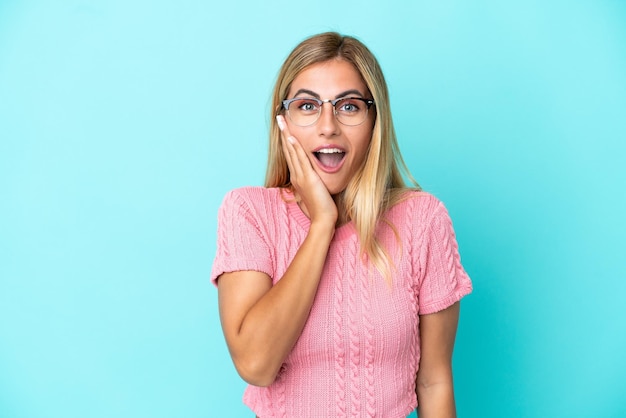 Blonde Uruguayan girl isolated on blue background with surprise and shocked facial expression