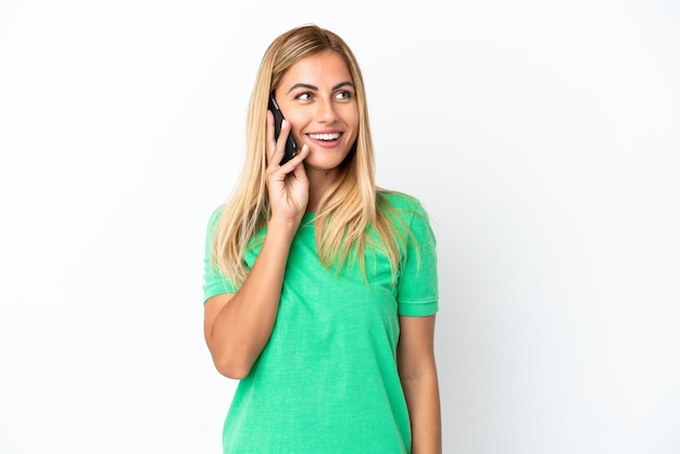 Blonde Uruguayan girl isolated on white background keeping a conversation with the mobile phone