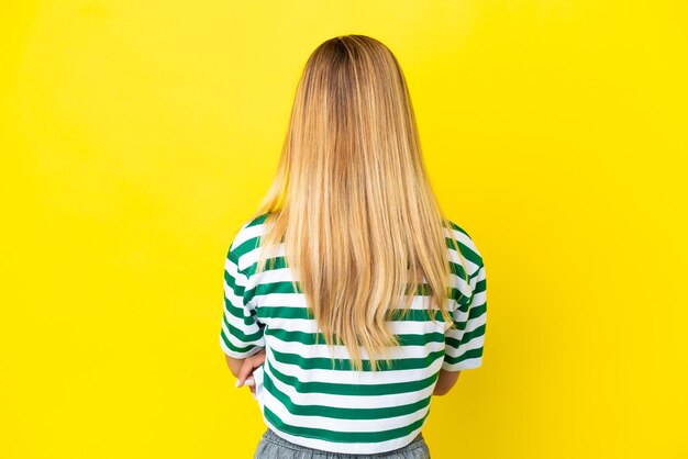 blonde uruguayan girl isolated on yellow background in back position