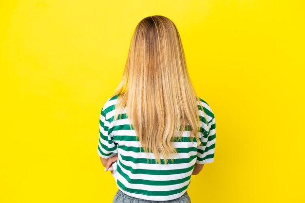 Blonde uruguayan girl isolated on yellow background in back position