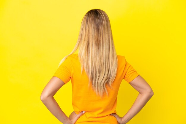 Blonde Uruguayan girl isolated on yellow background in back position