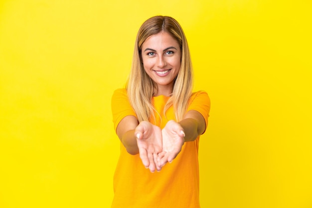 Blonde Uruguayan girl isolated on yellow background holding copyspace imaginary on the palm to insert an ad