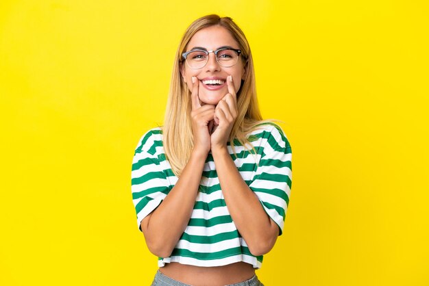 Blonde Uruguayan girl isolated on yellow background smiling with a happy and pleasant expression