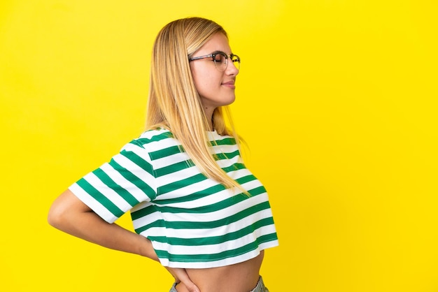 Blonde Uruguayan girl isolated on yellow background suffering from backache for having made an effort
