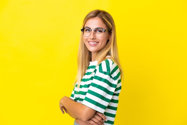 Ragazza bionda uruguaiana isolata su sfondo giallo con le braccia incrociate e guardando avanti