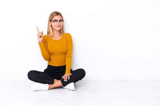 Blonde Uruguayan girl sitting on the floor pointing with the index finger a great idea