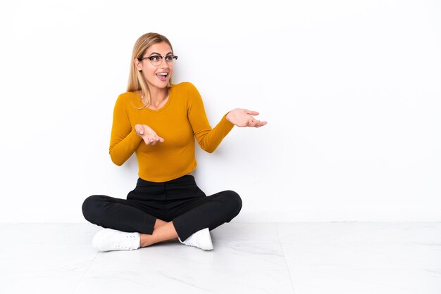 Blonde Uruguayan girl sitting on the floor with surprise facial expression