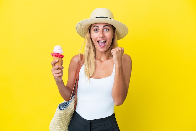 여름에 금발 우루과이 소녀가 우승자 위치에서 승리를 축하하는 노란색 배경에 고립 된 아이스크림을 들고