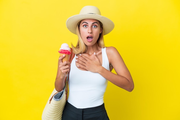 Blonde Uruguayan girl in summertime holding ice cream isolated on yellow background surprised and shocked while looking right