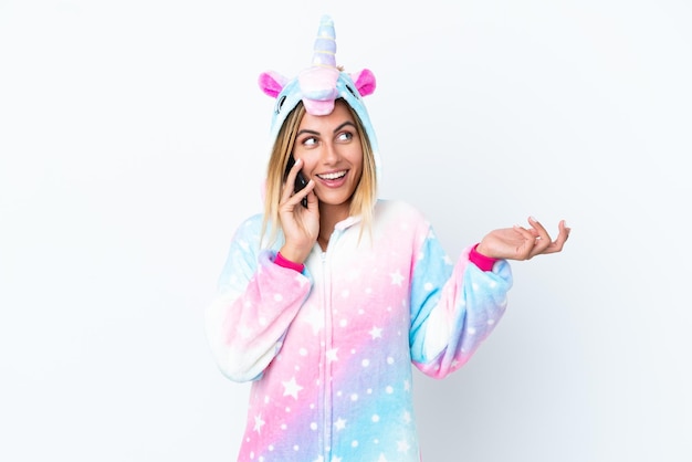 Blonde Uruguayan girl wearing a unicorn pajama isolated on white background keeping a conversation with the mobile phone with someone