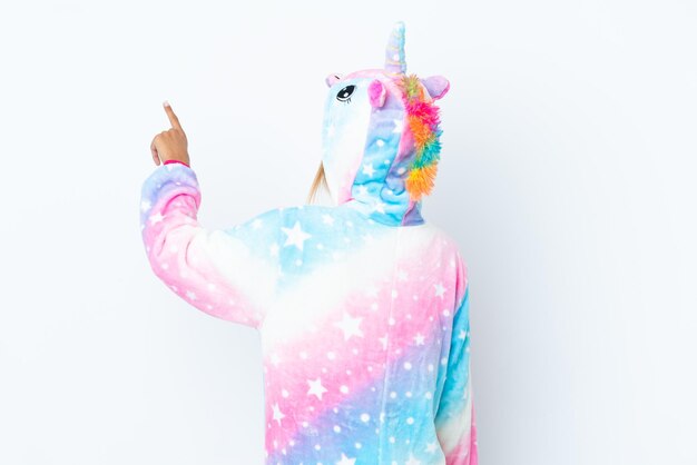 Photo blonde uruguayan girl wearing a unicorn pajama isolated on white background pointing back with the index finger