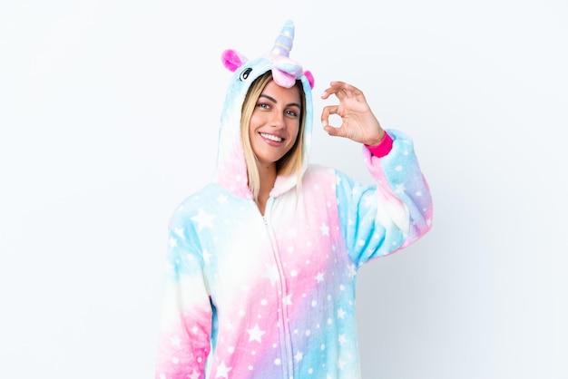 Blonde Uruguayan girl wearing a unicorn pajama isolated on white background showing ok sign with fingers