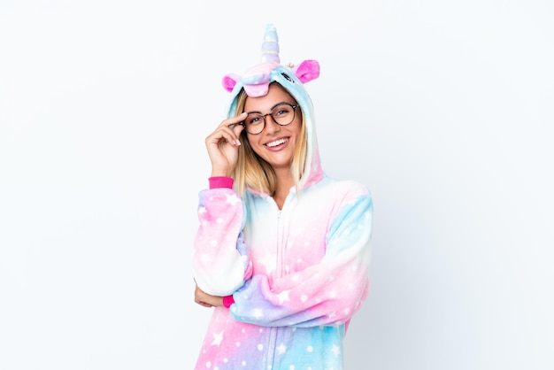Blonde Uruguayan girl wearing a unicorn pajama isolated on white background with glasses and happy