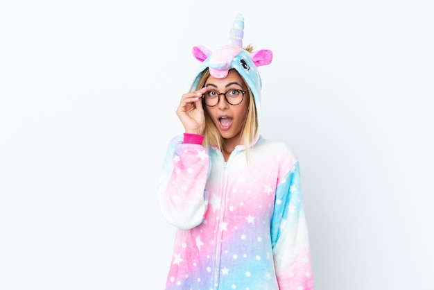 Blonde Uruguayan girl wearing a unicorn pajama isolated on white background with glasses and surprised