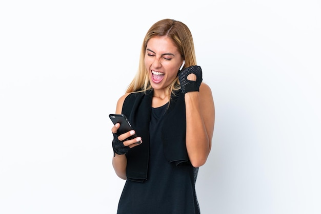 Blonde Uruguayan sport girl isolated on white background with phone in victory position