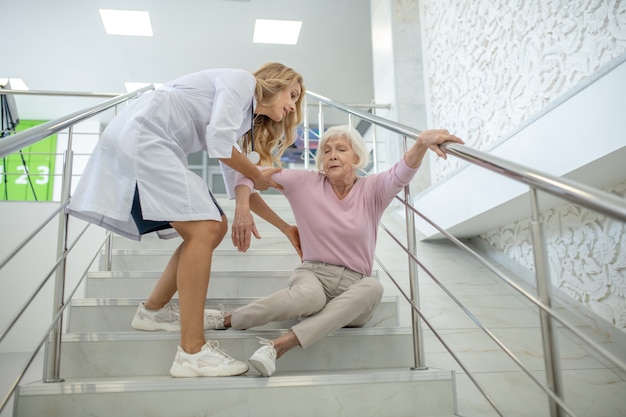 blonde verpleegster die de oudere vrouw hielp die op de strairs viel