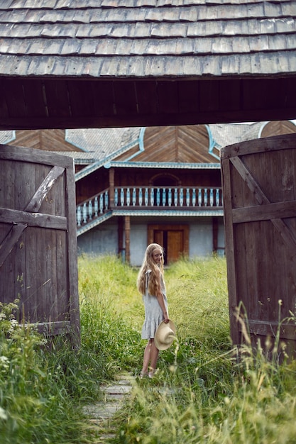 Foto una ragazza di villaggio bionda con i capelli lunghi si trova in un cancello di legno nel villaggio in estate