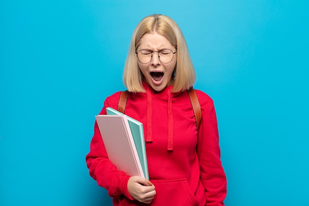 Blonde vrouw die agressief schreeuwt, erg boos, gefrustreerd, verontwaardigd of geïrriteerd kijkt en nee schreeuwt