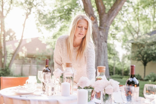 Blonde vrouw die een tafel dekt in een tuinvazen met roze rozen