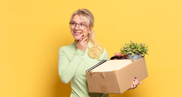 Blonde vrouw die gelukkig glimlacht en dagdroomt of twijfelt, kijkend naar de kant