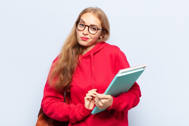 Blonde vrouw die haar schouders ophaalt, zich verward en onzeker voelt, twijfelt met gekruiste armen en verbaasde blik