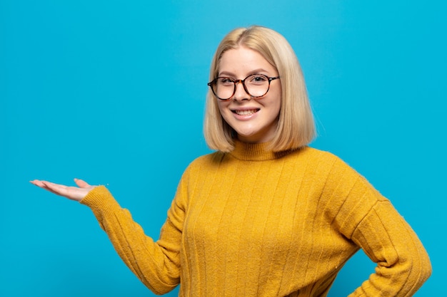 blonde vrouw die lacht, zich zelfverzekerd, succesvol en gelukkig voelt, concept of idee toont op kopie ruimte aan de zijkant