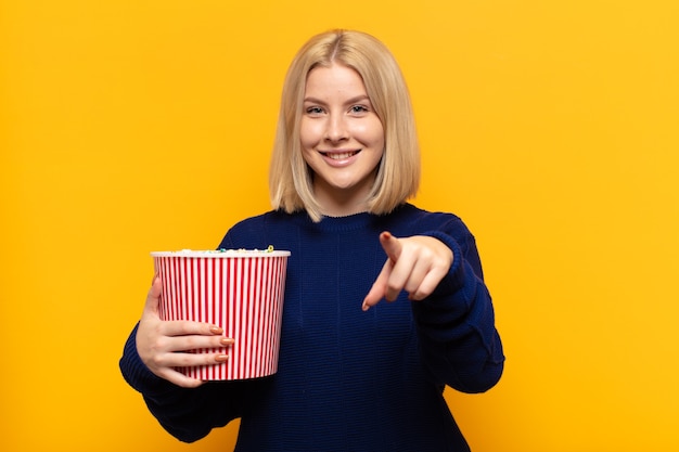 Blonde vrouw die naar voren wijst met een tevreden, zelfverzekerde, vriendelijke glimlach, die jou kiest