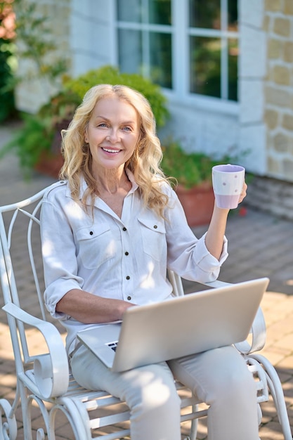 Blonde vrouw die op internet surft terwijl ze haar ochtendkoffie drinkt