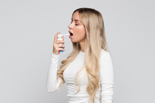 Blonde vrouw die spray gebruikt om keelpijn te behandelen.