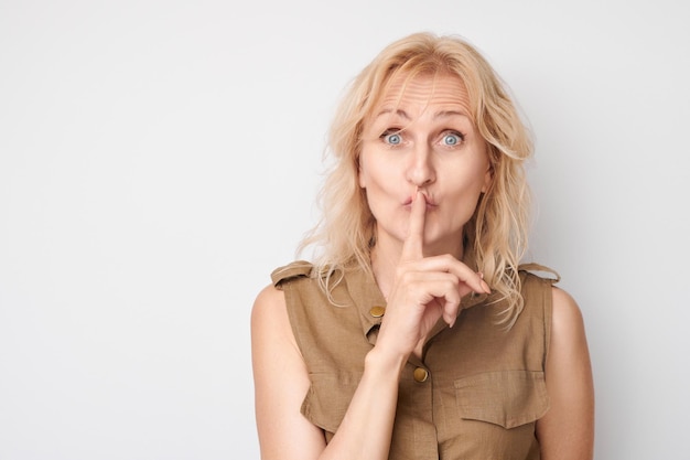 Blonde vrouw die stilte gebaar met vinger op lippen geïsoleerd op witte achtergrond