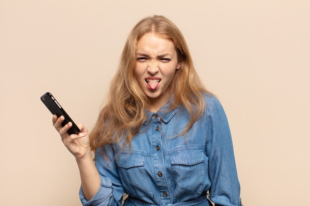 Blonde vrouw die walgt en geïrriteerd is, tong uitsteekt, niet van iets smerigs en vies houdt