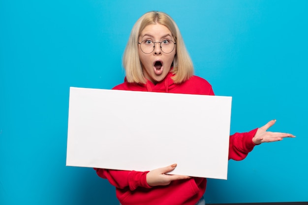 Foto blonde vrouw die zich extreem geschokt en verrast, angstig en in paniek voelt, met een gestreste en geschokte blik