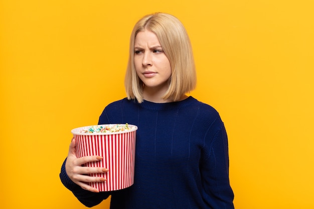 Blonde vrouw die zich verdrietig, boos of boos voelt en opzij kijkt met een negatieve houding, fronsend van onenigheid