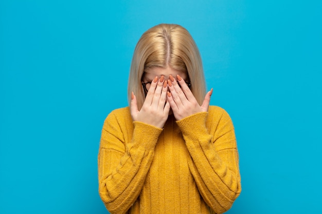 Blonde vrouw die zich verdrietig, gefrustreerd, nerveus en depressief voelt, haar gezicht met beide handen bedekt, huilt