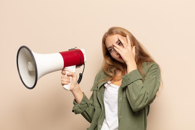 Blonde vrouw die zich verveeld, gefrustreerd en slaperig voelt na een vermoeiende, saaie en vervelende taak, gezicht met hand vasthoudend