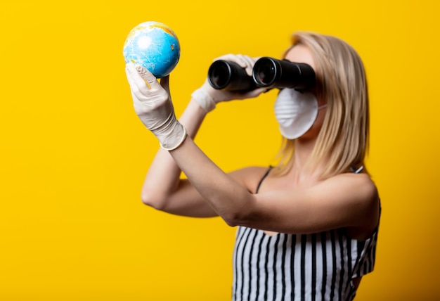Blonde vrouw in gezichtsmasker en handschoenen houdt Earth globe en verrekijker
