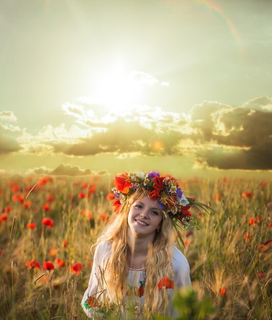 Blonde vrouw in het tarweveld met papaver op de zonsondergang